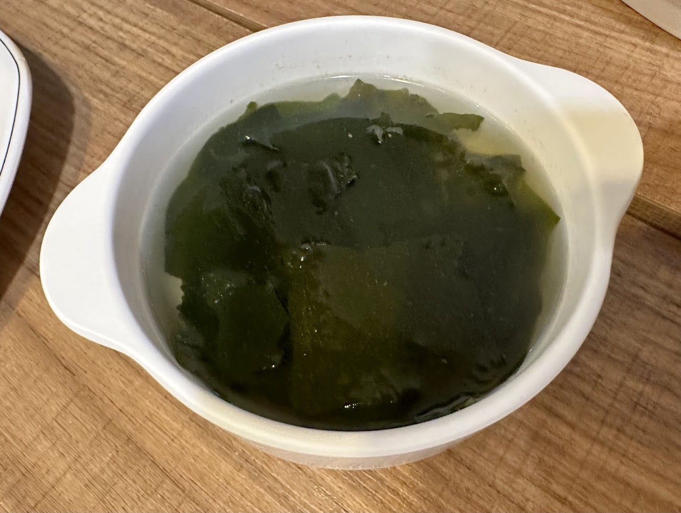 圖片中是一碗以白色碗盛裝的海帶湯，湯內主要有大片深綠色的海帶，湯色透明，整體簡單且清爽。