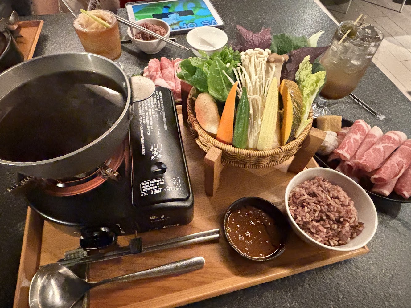 套餐桌上的火鍋料理，有蔬菜拼盤、肉片、紫米飯、醬料和飲料
