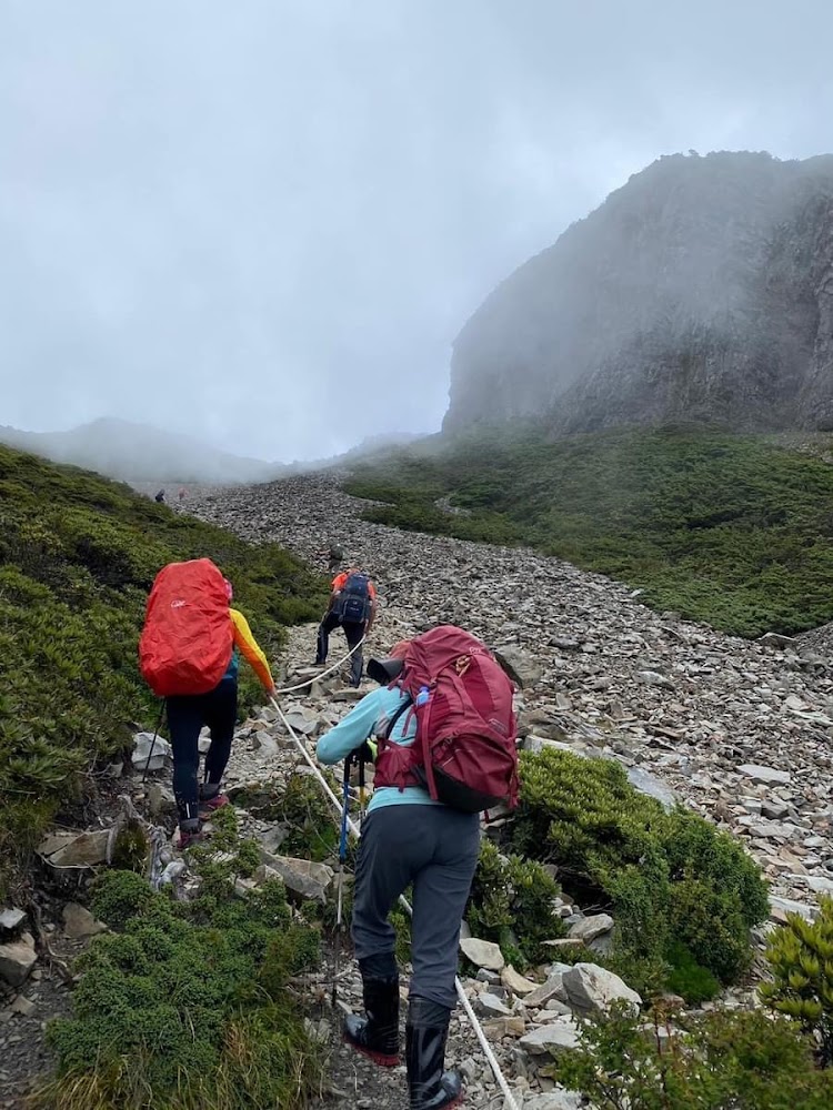 數名登山者背著大背包在石坡上攀爬