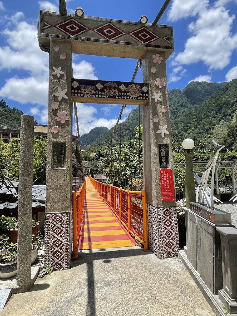明治溫泉老街橋頭,石柱刻原住民菱形紋飾和粉色花朵,橋面橘紅條紋