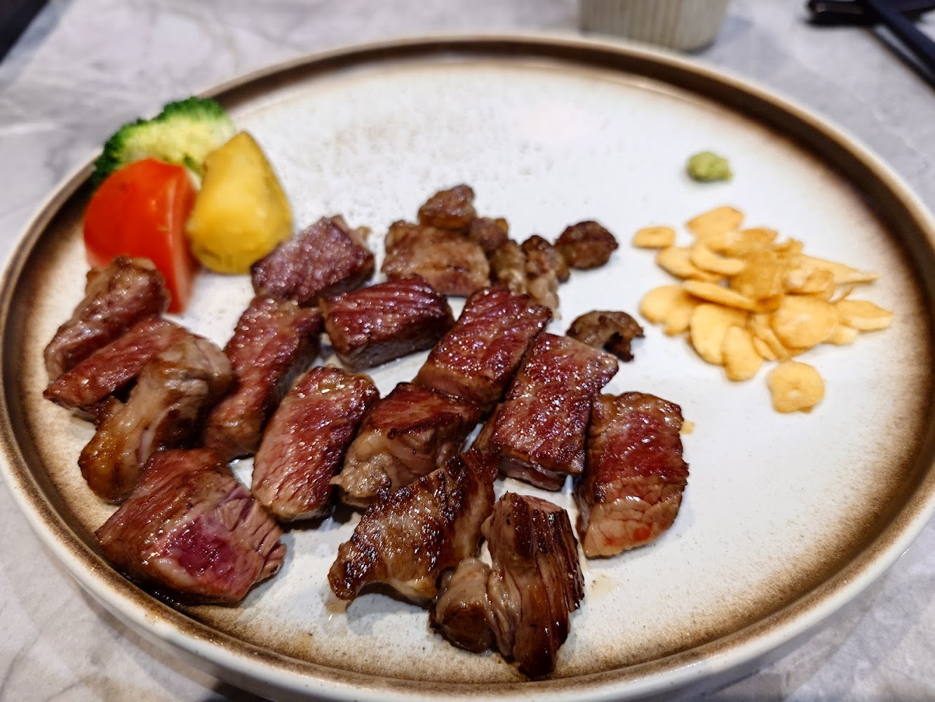 這張圖片主要展示了一盤鐵板牛排，切成一塊塊的牛肉，配有蒜片、芥末和一些蔬菜如番茄、花椰菜及馬鈴薯。擺盤精緻，色香誘人。