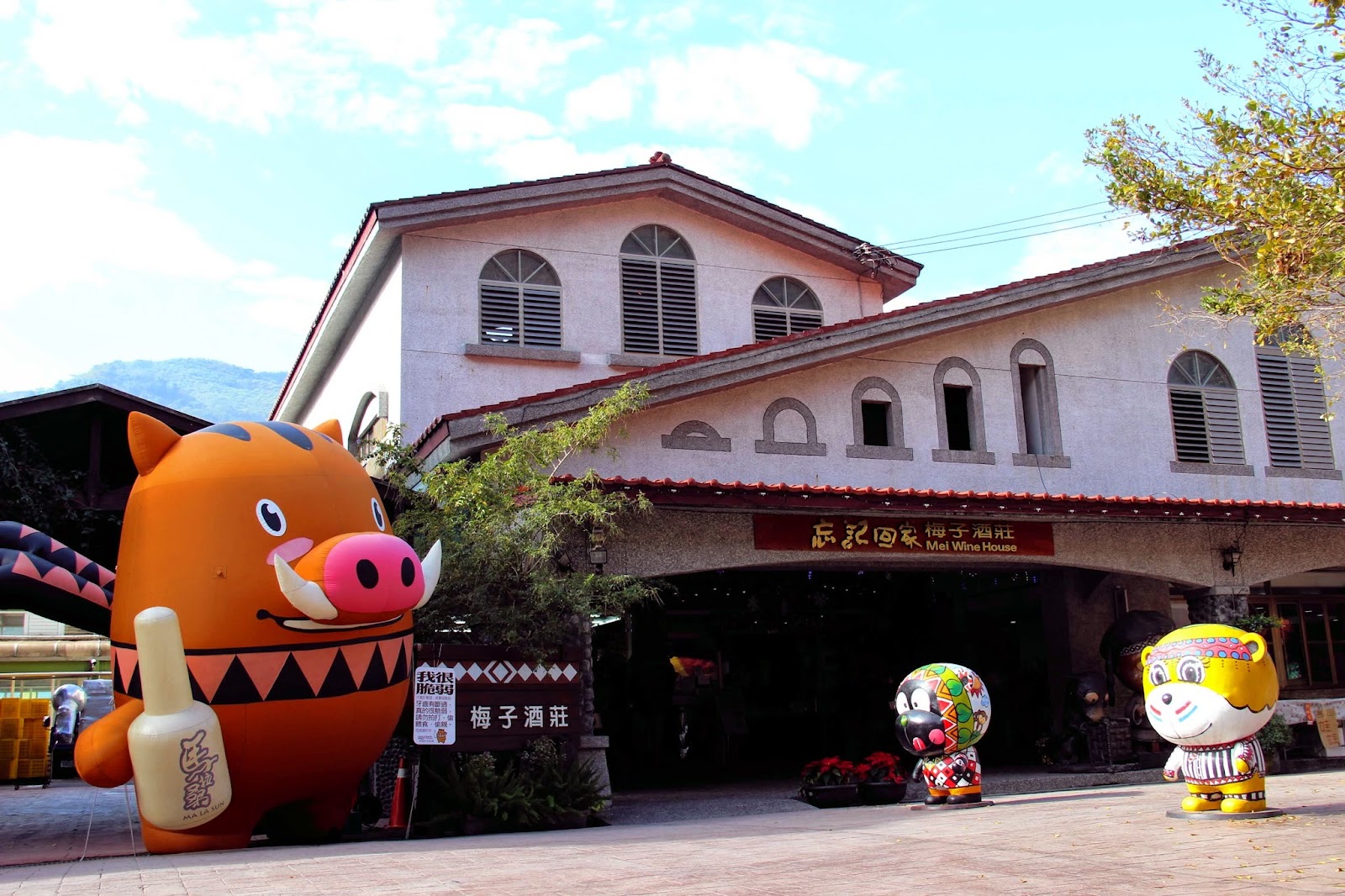 梅子夢工廠歐式白色建築外觀，前方擺有布農族風格的原住民卡通公仔