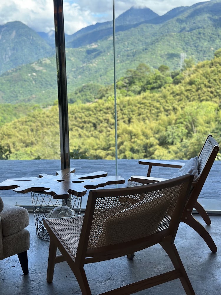 室內靠窗座位區，有木質椅子與造型茶几，窗外是綠色山景