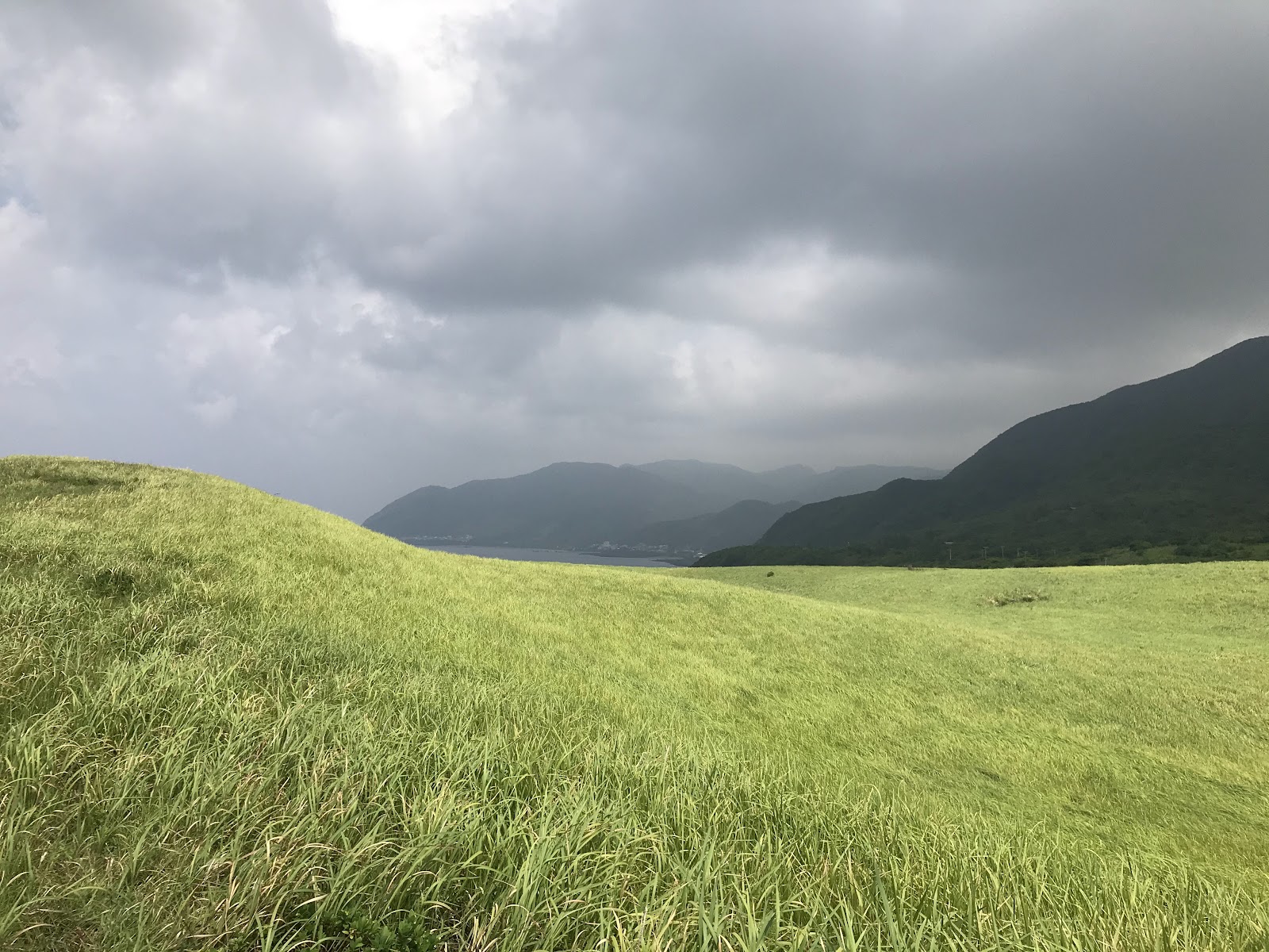 蘭嶼青青草原翠綠草坡連綿起伏遠方山巒海灣烏雲光線穿透壯麗景色
