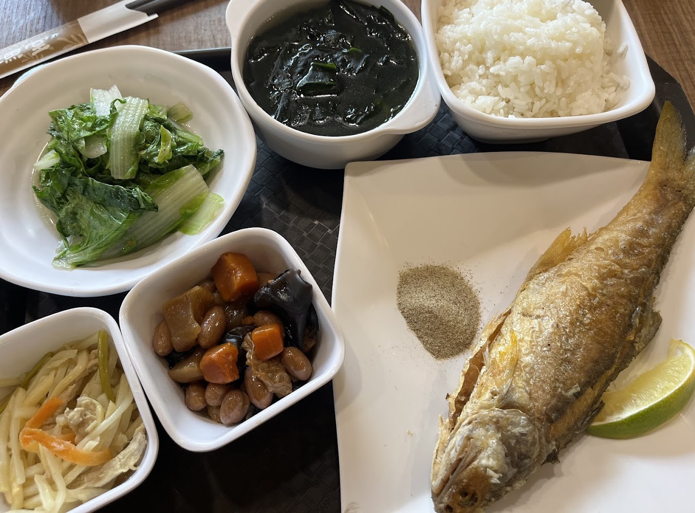 這是一份包含炸魚、白飯、海帶湯、炒青菜、豆乾小菜和涼拌菜的中式套餐，看起來營養均衡且豐富。