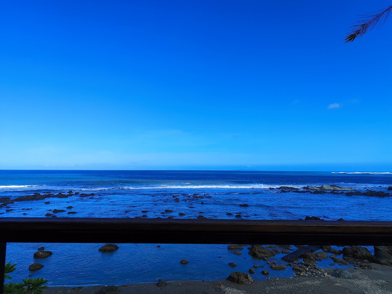 蔚藍海洋與礁石海岸，前方沙灘散布岩石