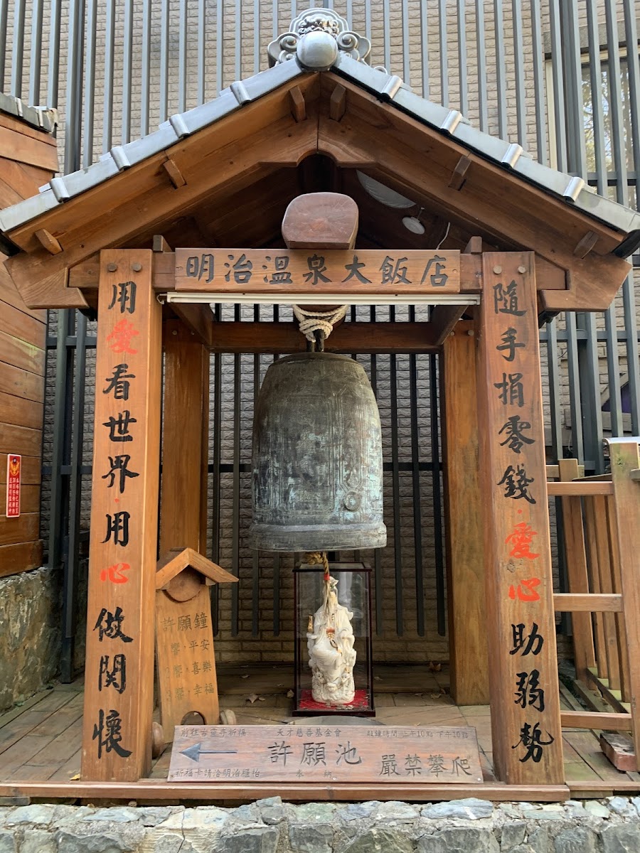明治溫泉大飯店入口許願鐘亭,銅鐘懸掛於木製閣樓,紅字楹聯,底部觀音白瓷像