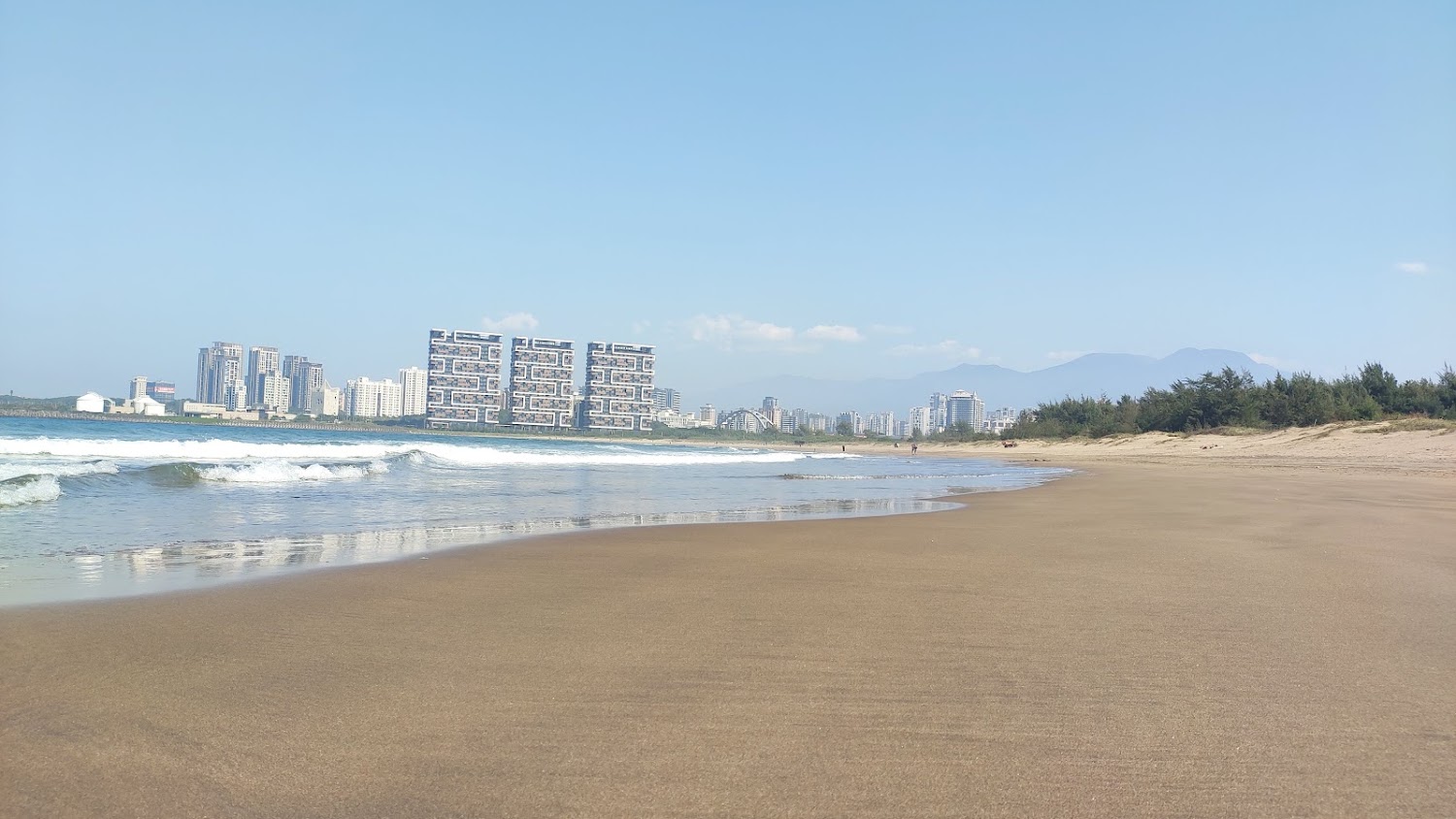 寬廣沙灘、海浪與遠方現代建築群的沙崙海水浴場白天景色
