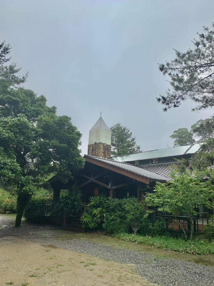 這張圖片主要是戶外一座被綠樹和植物環繞的小屋，屋頂有一個石造的尖塔，整體環境安靜自然，營造出寧靜舒適的氛圍。