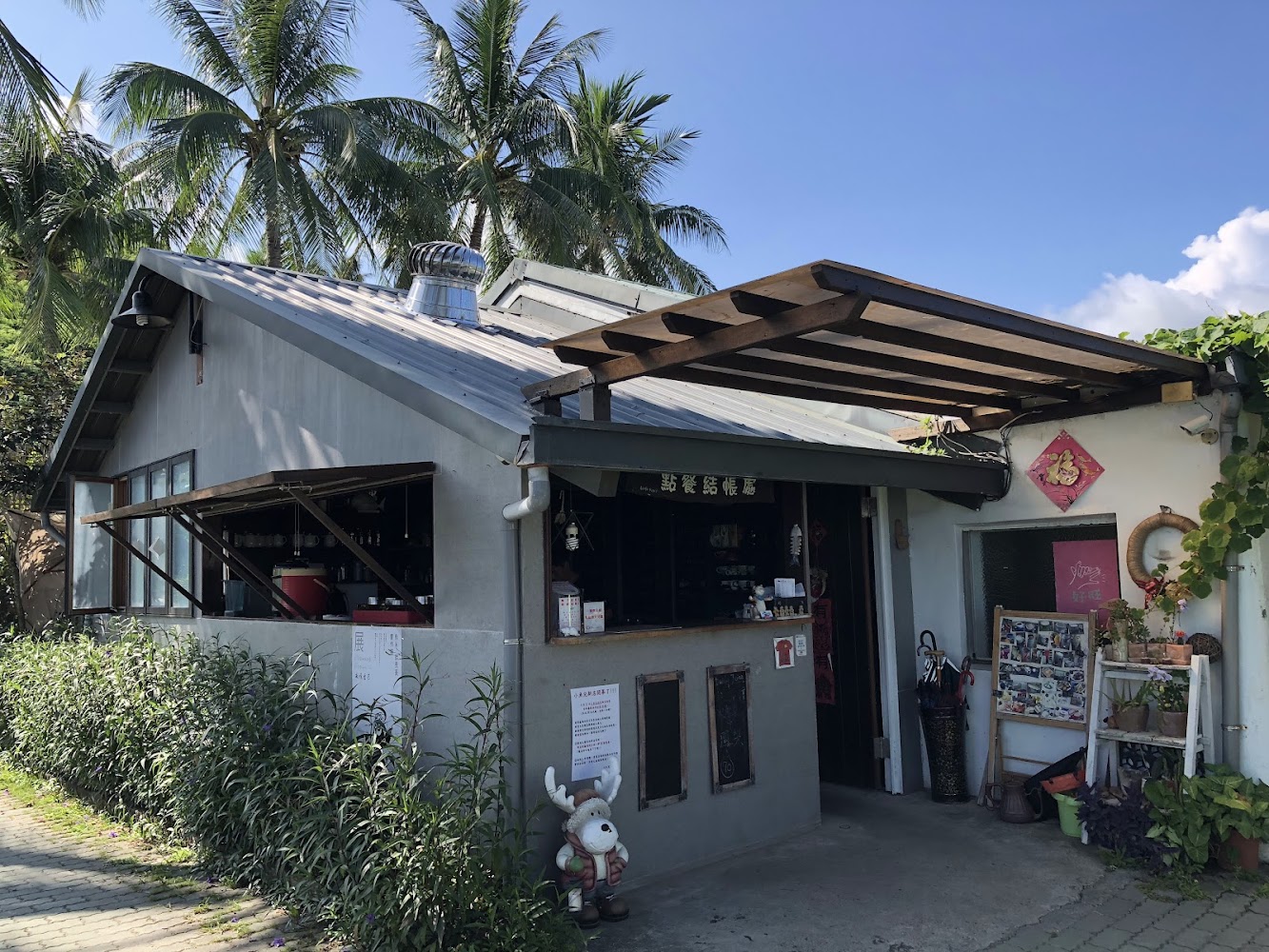 位於熱帶地區的小店，屋外有綠植和椰子樹，店前擺放著公仔、小黑板和各類裝飾