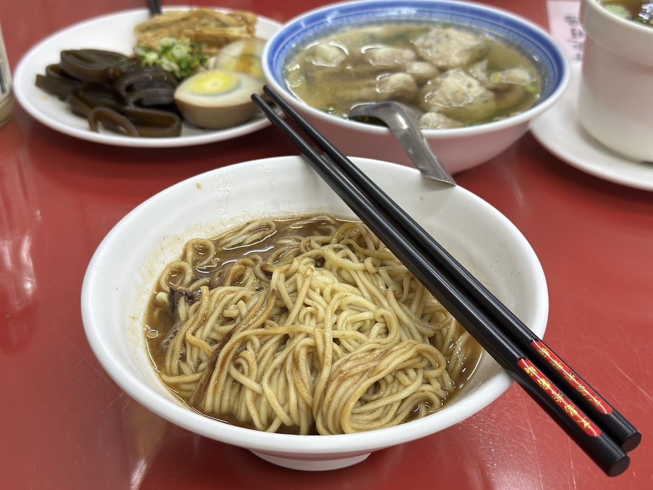 一碗乾拌麵，旁邊有餛飩湯與滷味拼盤