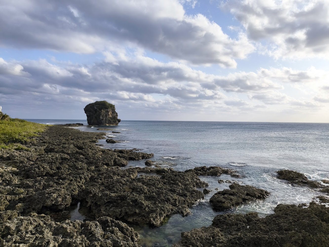 海岸景觀有大片礁石與平靜海面，遠方有孤立大岩石