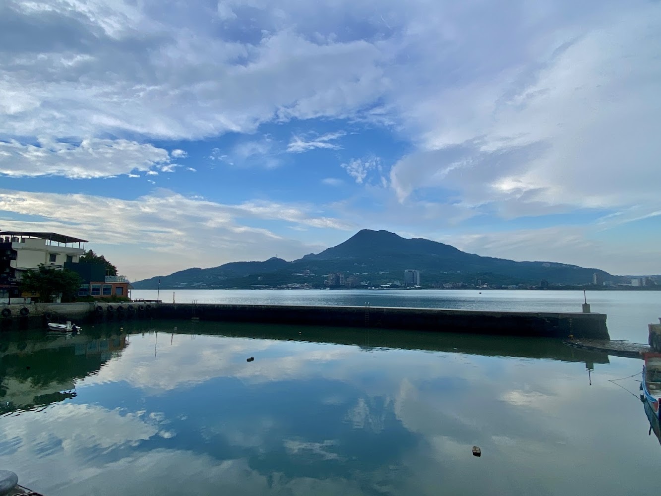平靜海港與遠方山脈，天空與雲彩倒映在水面