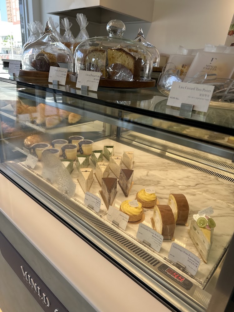 這張圖片展示了一家咖啡店的甜點櫃,裡面有多種不同的蛋糕、塔和麵包,包括千層蛋糕、磅蛋糕和奶油塔,每個甜點都有標示牌,外觀看起來精緻誘人。