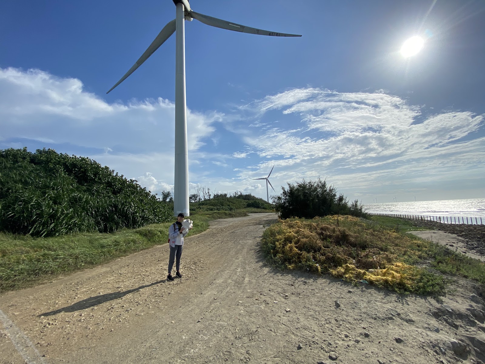 新竹17公里海岸線風力發電機，遊客站在沿海土路旁，右側是台灣海峽