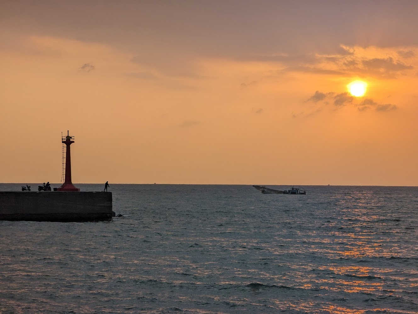 海邊碼頭紅色燈塔與夕陽下釣魚的人