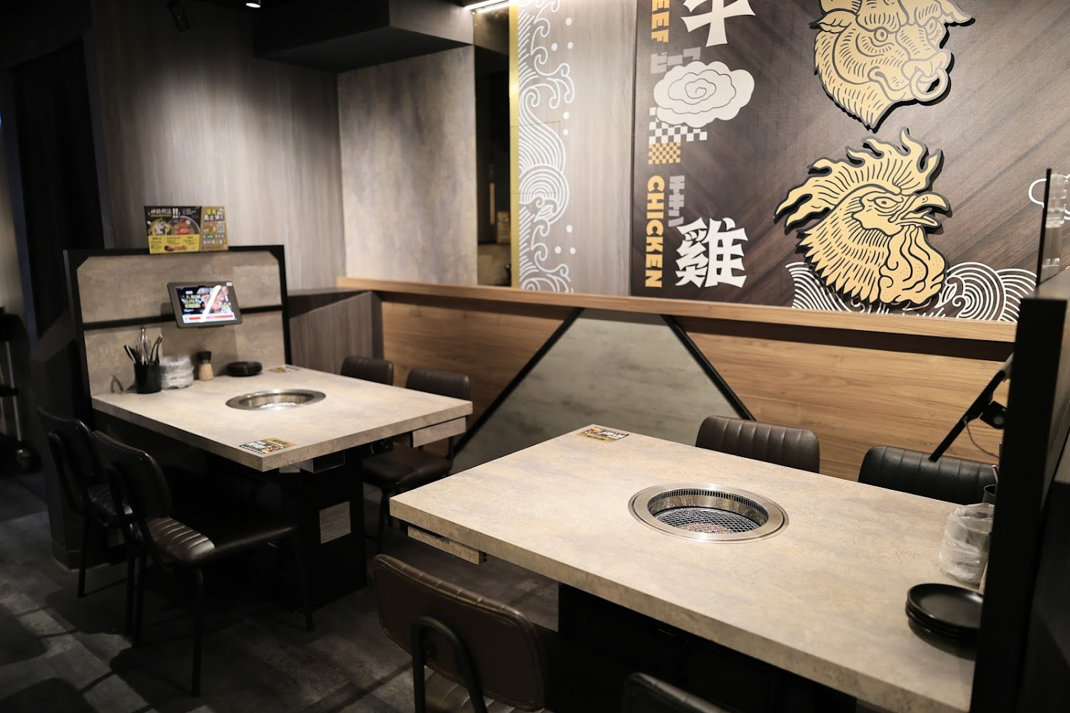 日式燒肉餐廳桌上有烤爐、點餐平板，牆上有牛和雞的圖案及文字
