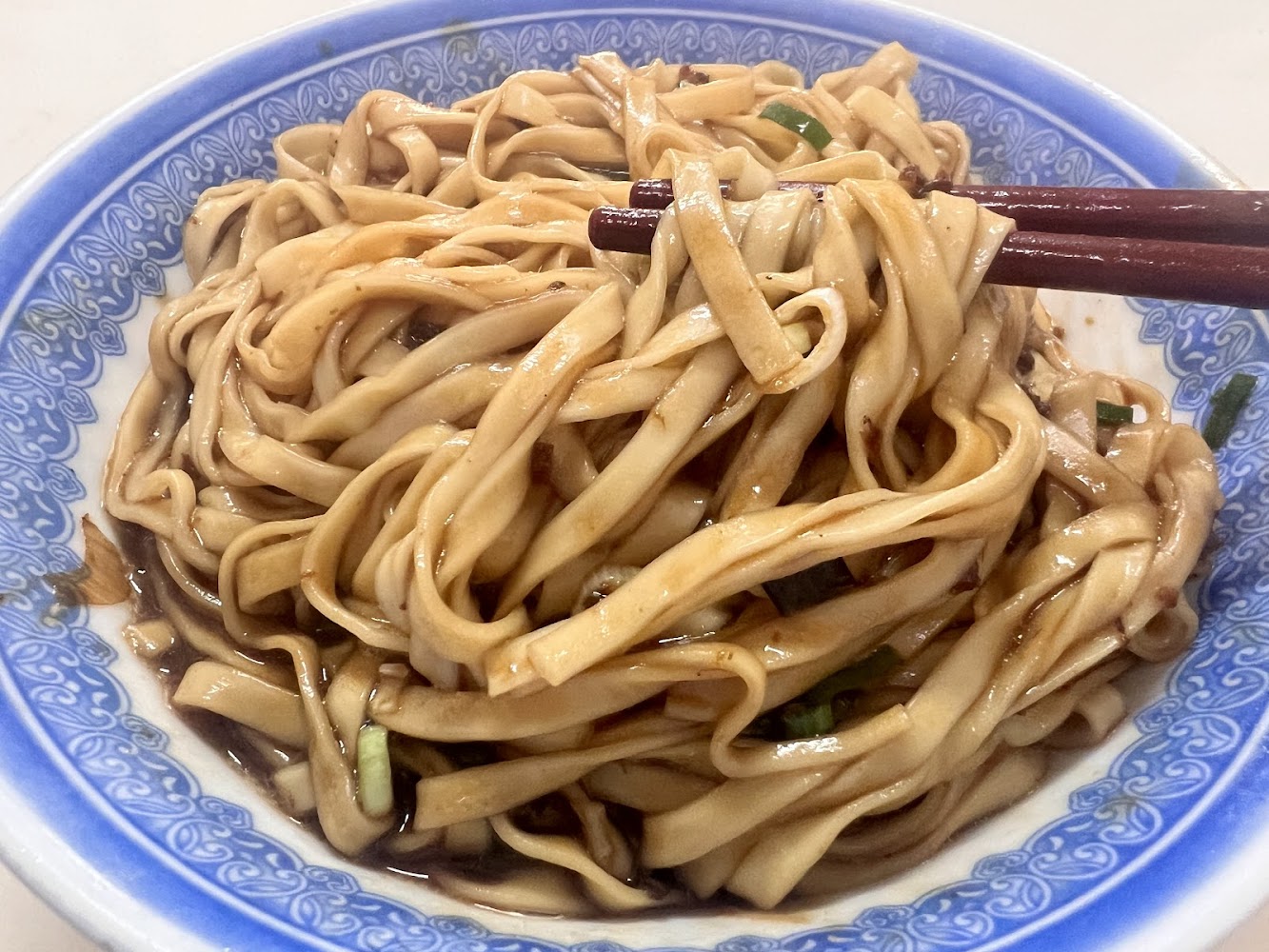 一碗用醬汁拌過的寬麵條，麵條上帶有些許蔥花