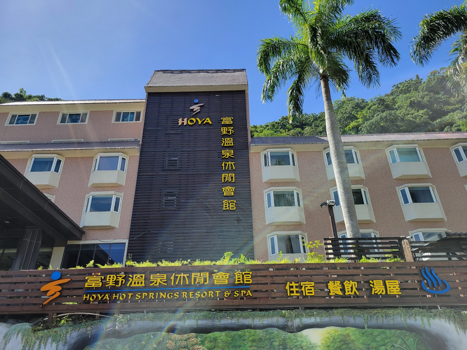 富野溫泉休閒會館HOYA外觀，黑色木質外牆金字招牌，棕櫚樹，藍天山景