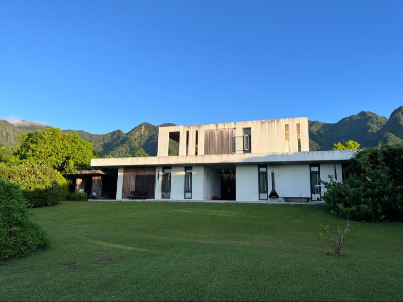 聽風說故事民宿建築外觀,現代木造建築座落翠綠草坪,背景為山脈