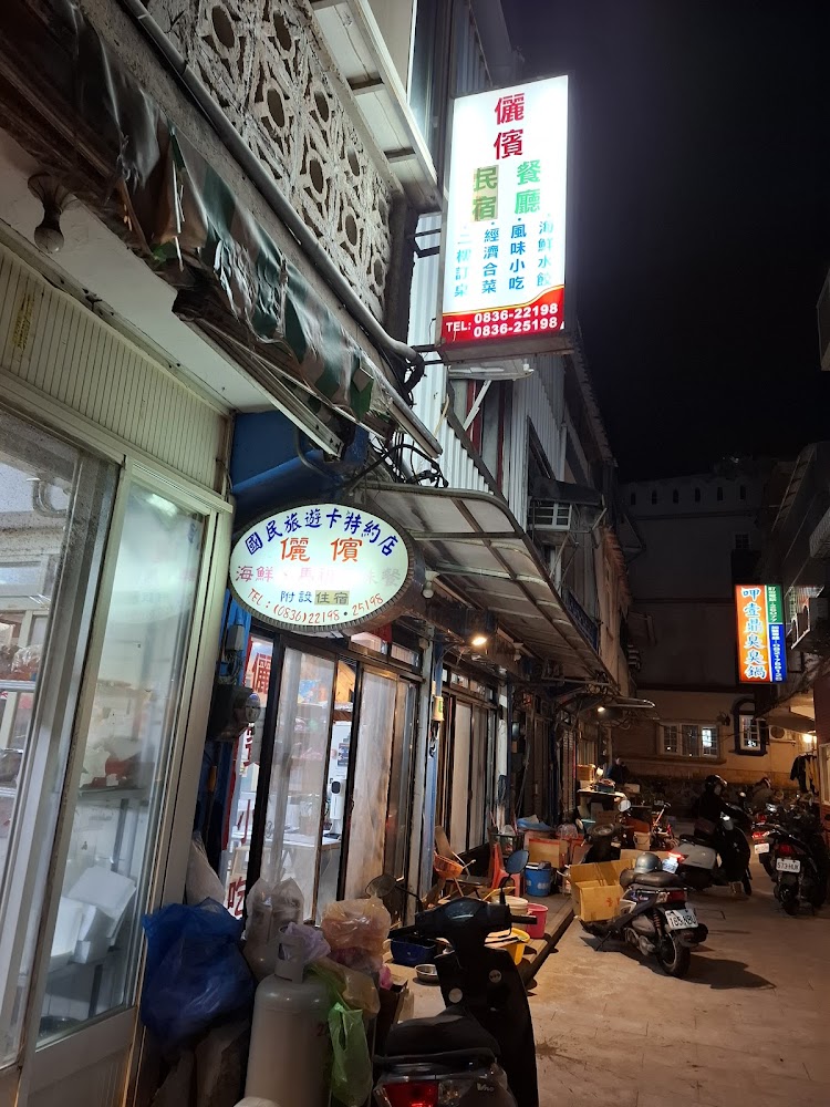 這張圖片展示一條夜晚的小巷，巷內有多間餐廳及民宿，店家門口擺放各種雜物和機車，招牌明亮顯眼，營造出熱鬧的夜市氛圍。