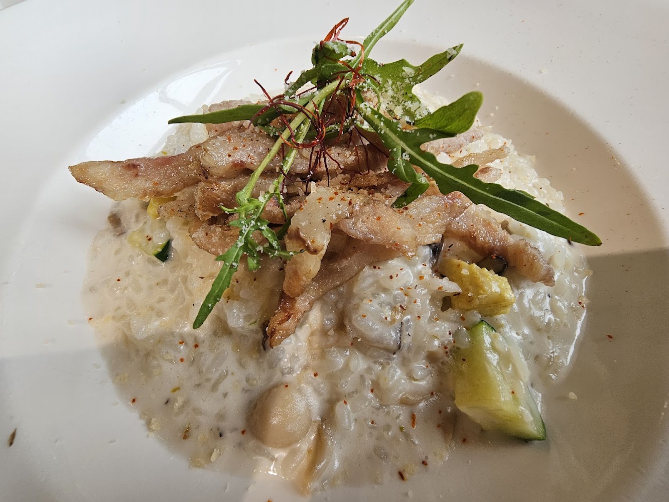 奶油燉飯上方有炸過的肉片，點綴新鮮蔬菜與香草