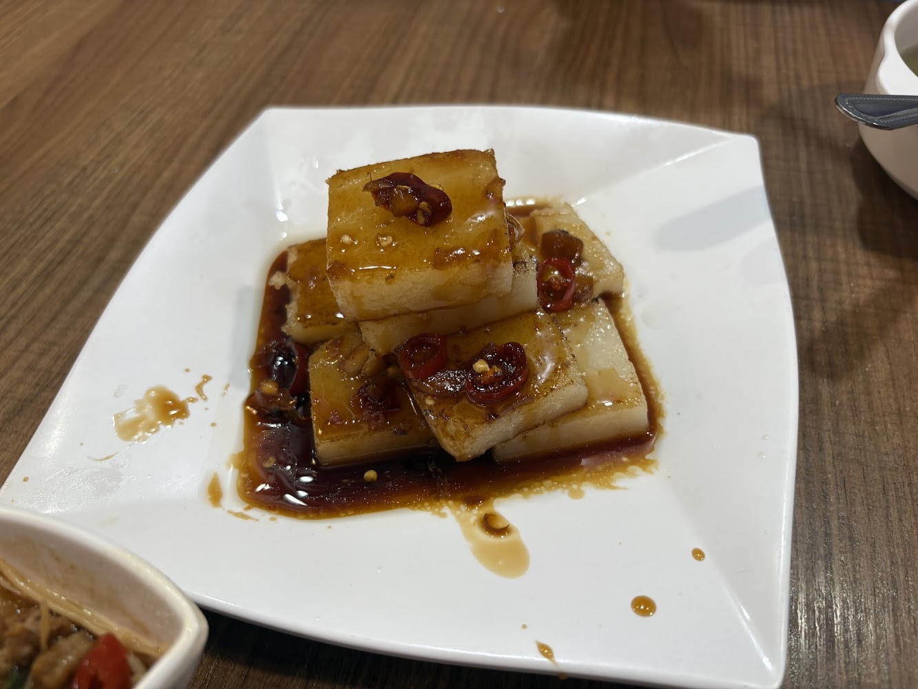 這張圖片主要是一盤擺放整齊的蘿蔔糕，上面淋有醬油和辣椒片，看起來香辣可口，是一道常見的中式小吃。
