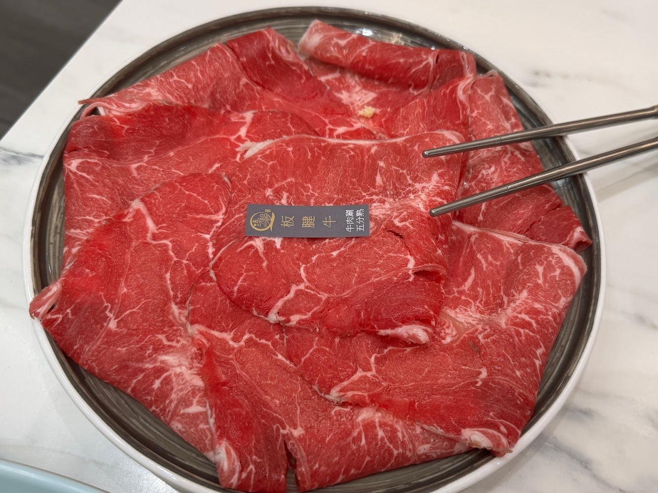 一盤新鮮切片牛肉，油花分布均勻。