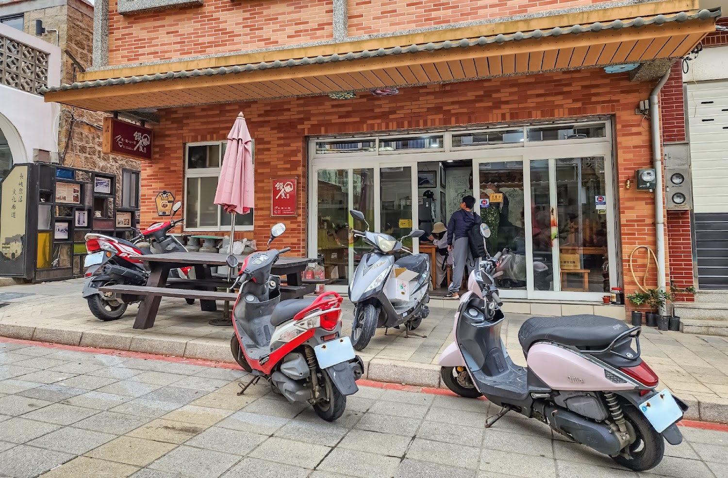 紅磚牆面的店家門口，門外有機車與戶外桌椅