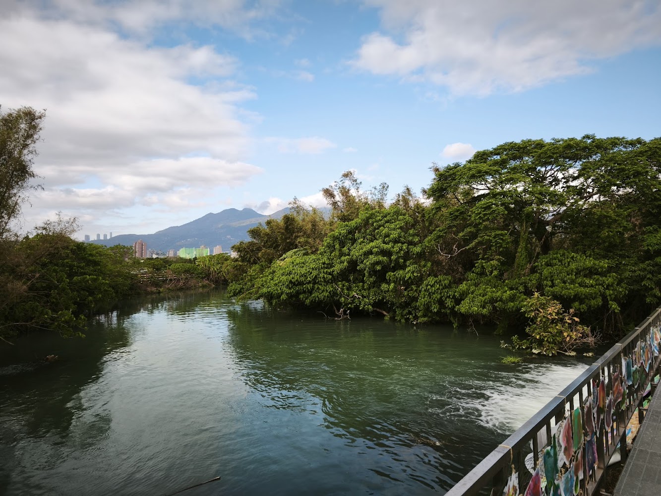 河道兩側綠樹茂密遠方有山景與城市欄杆彩繪