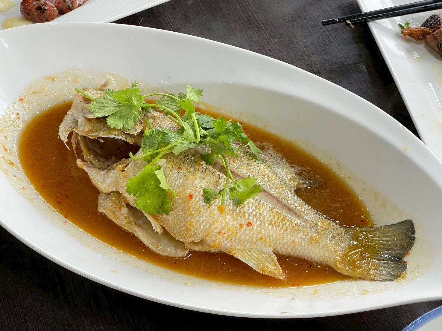 清蒸魚完整上桌，表面有香菜裝飾