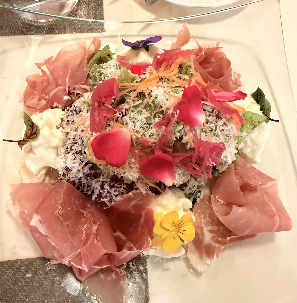 一道擺盤精美的沙拉，包含生火腿片、綠色蔬菜、起司、食用花瓣及蔬菜絲