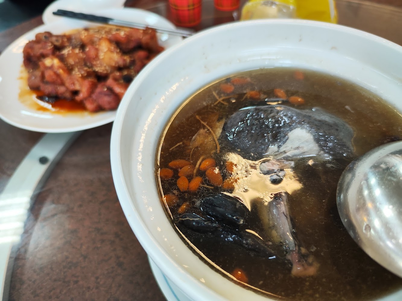 一道以烏骨雞、中藥材和枸杞燉煮的湯品，旁邊有一盤紅燒肉類料理