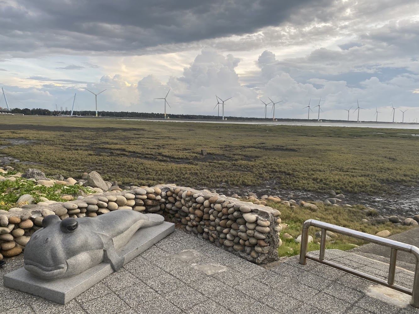 前景為彈塗魚雕像,後方濕地與風力發電機構成開闊景觀