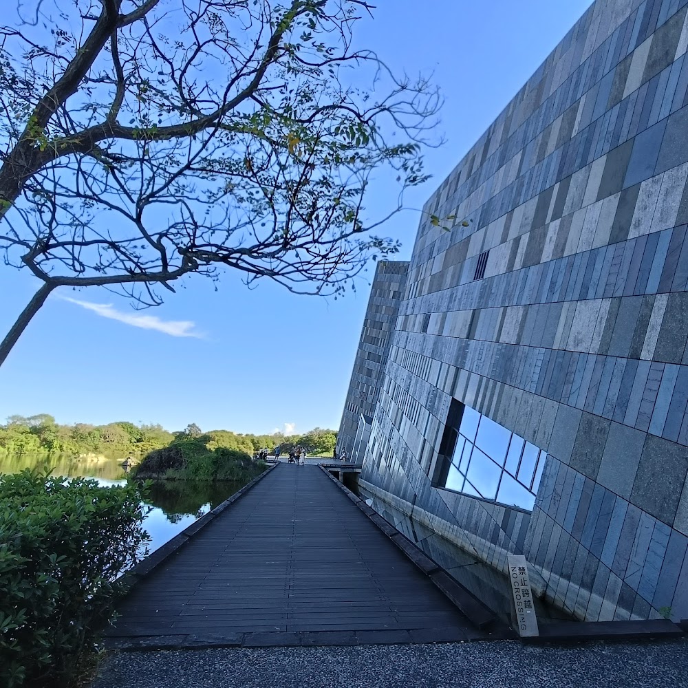 外觀現代的斜面建築旁有一排水面與木棧道，四周綠意盎然、藍天環繞
