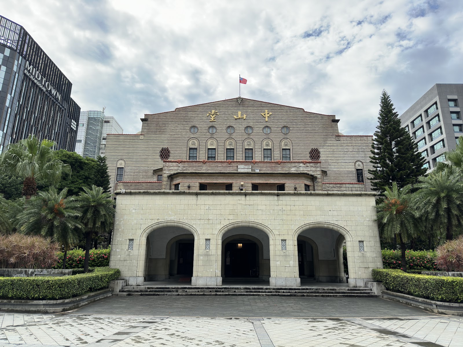 臺北市中山堂正面全景，灰白色歷史建築，金字中山堂招牌，三拱形入口，棕櫚樹環繞