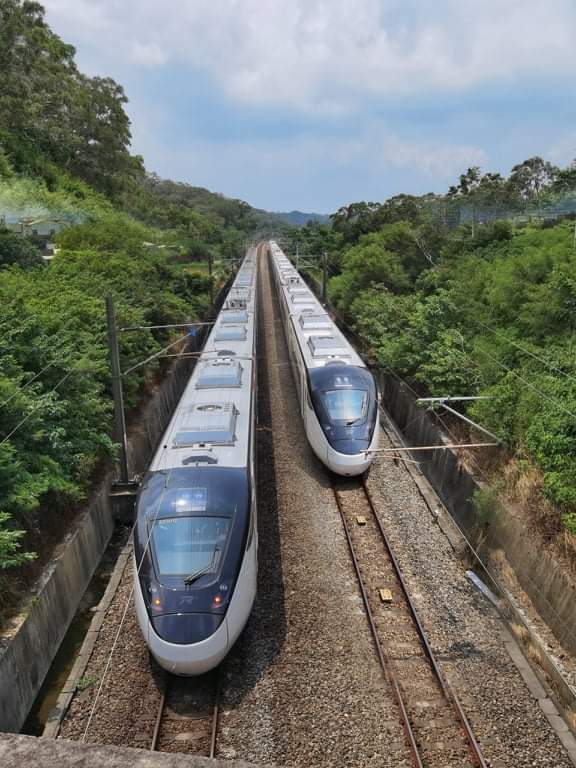 兩列高速列車分別行駛於兩條鐵軌，周圍綠樹環繞