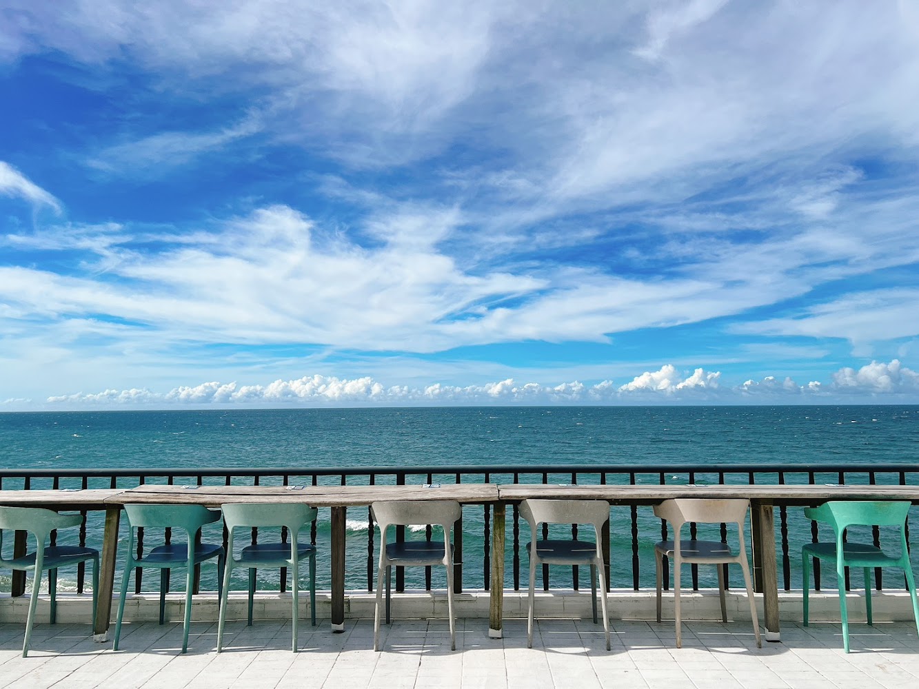 一排面向大海的桌椅，後方是無邊際海洋與晴朗天空