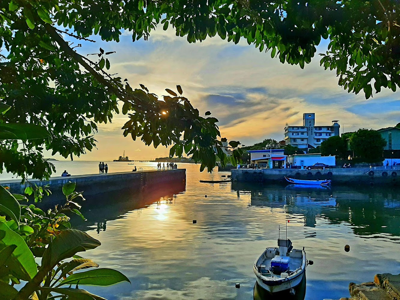 寧靜港口水面停著小船，夕陽映照，有人在碼頭散步