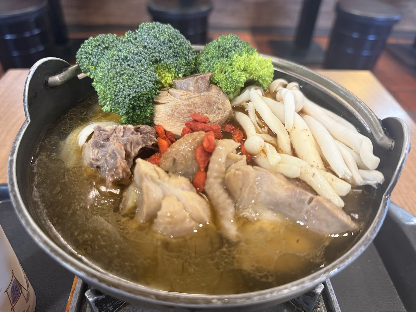 這張圖片顯示一鍋熱騰騰的湯品，裡面有花椰菜、白玉菇、肉塊和枸杞，食材豐富，湯頭清澈，呈現出健康美味的感覺。