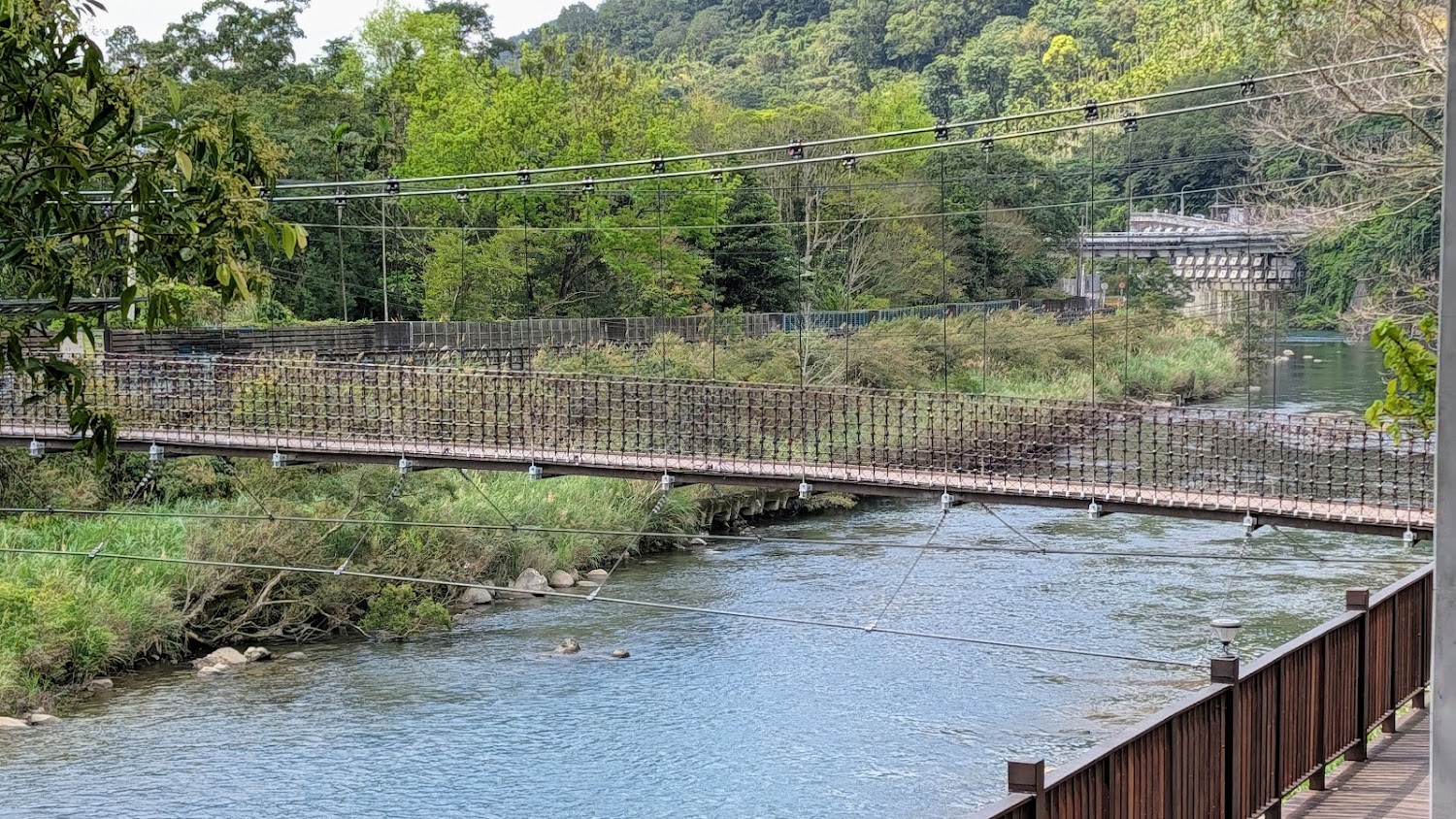 橫跨河流的吊橋，橋下是清澈溪流，兩岸綠意盎然