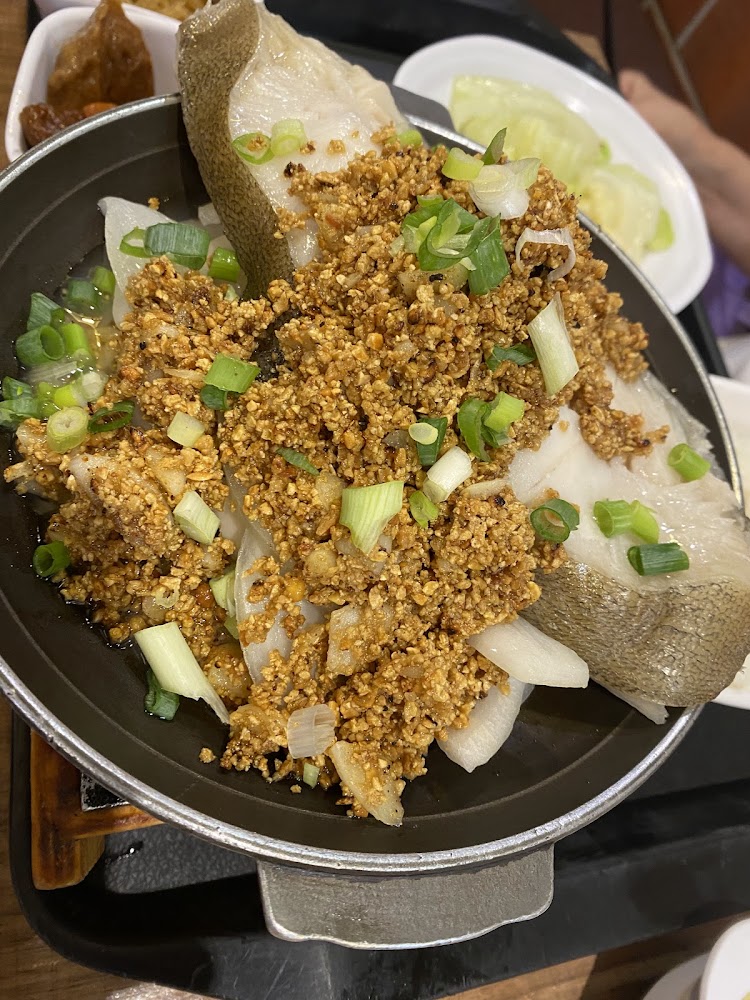 這張圖片主要是一道美食，主角是魚肉，上面鋪有大量蒜酥和蔥花，旁邊還有洋蔥。背景有配菜與蔬菜，色香味俱全。