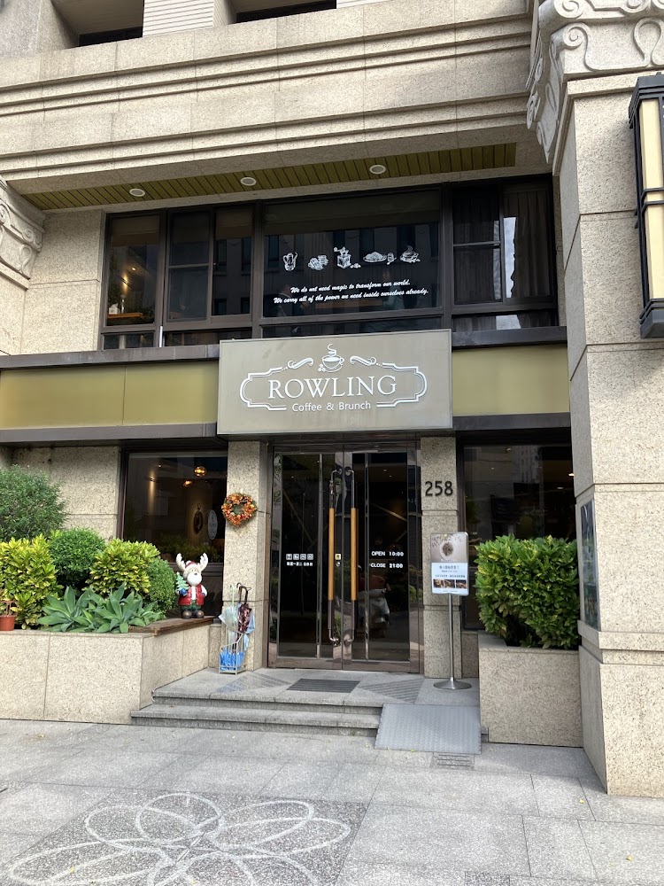 這是一間名為ROWLING Coffee & Brunch的咖啡廳門口，外觀溫馨。門前有綠色植栽、聖誕裝飾鹿和一個營業資訊看板，整體氣氛舒適且歡迎。