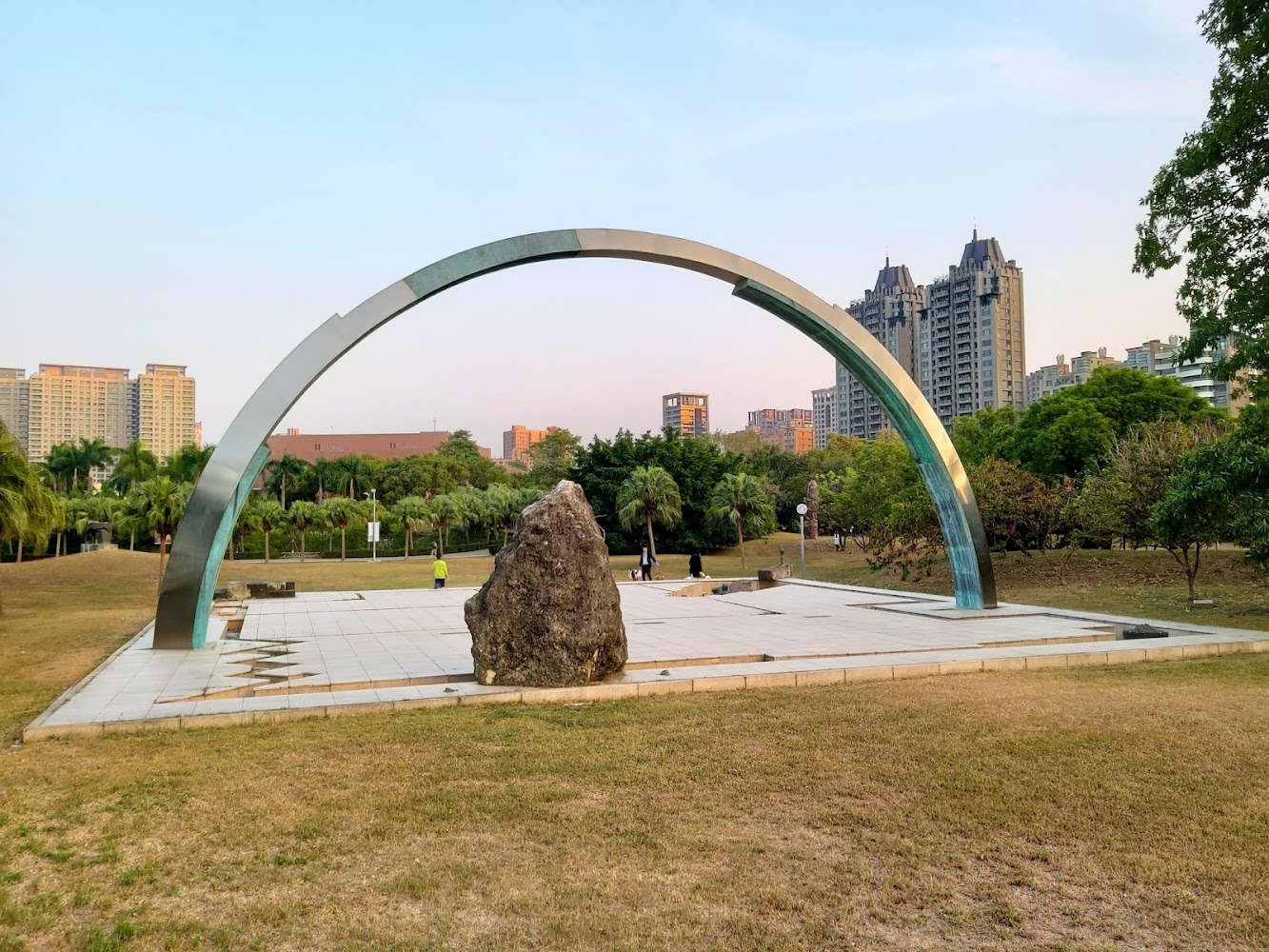 大型金屬圓弧雕塑與巨石位於草地廣場中央
