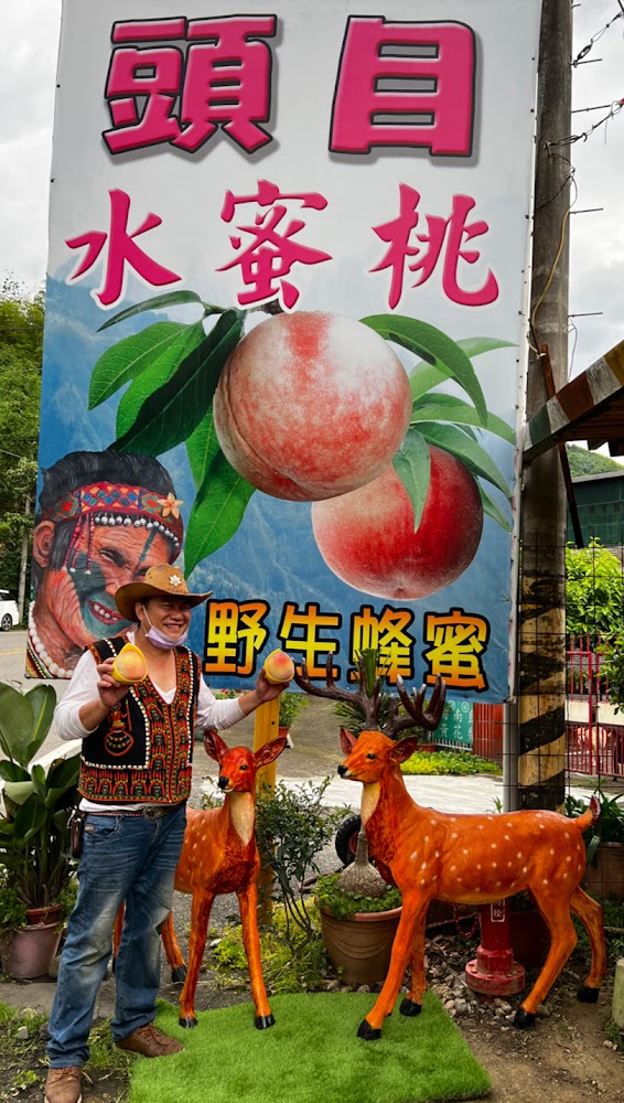 穿著原住民服飾的人手拿水蜜桃站在頭目水蜜桃招牌前