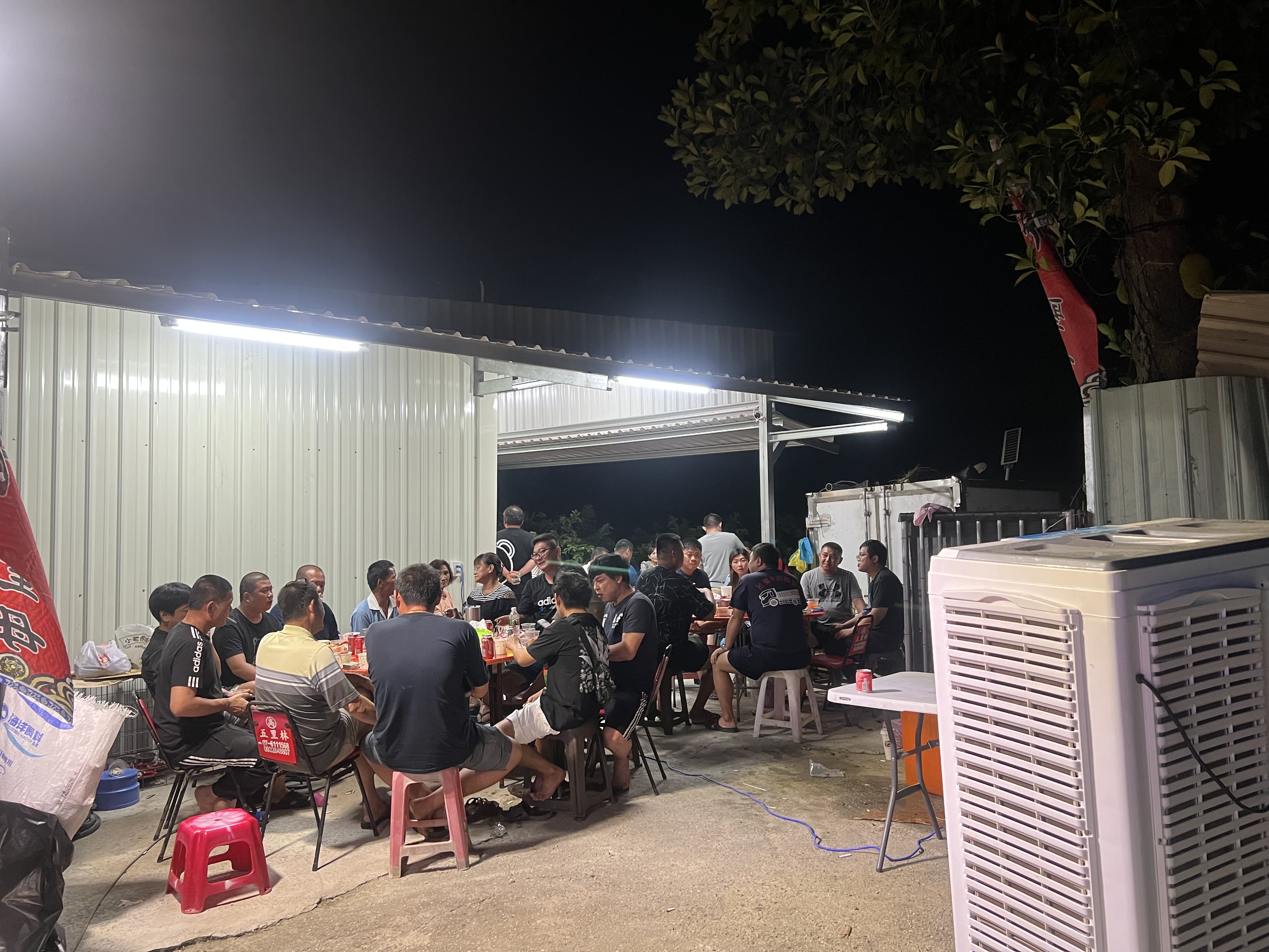 一群人在戶外長桌旁聚餐聊天，氣氛熱鬧