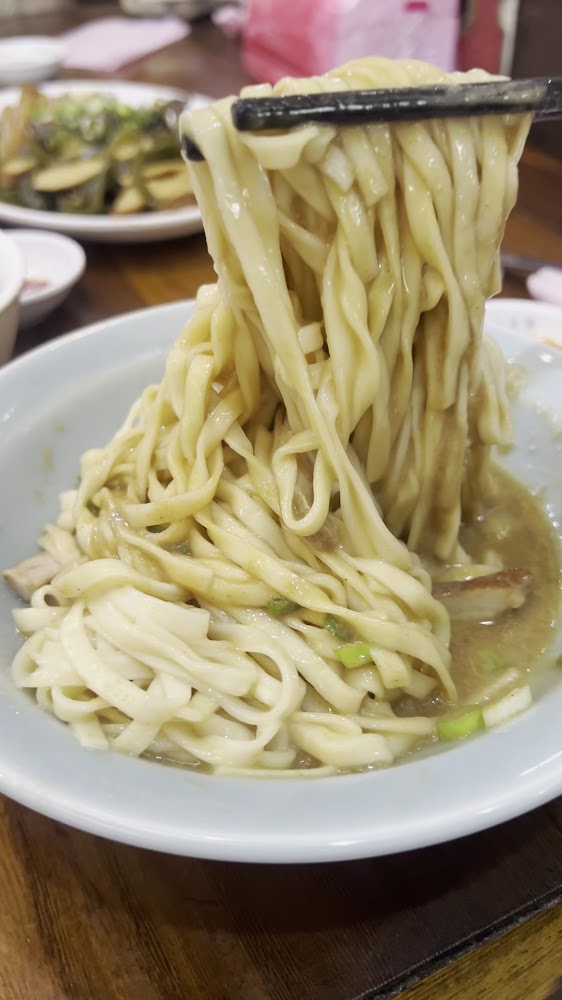 寬厚拌麵特寫，麵條裹上濃郁醬汁並被筷子夾起