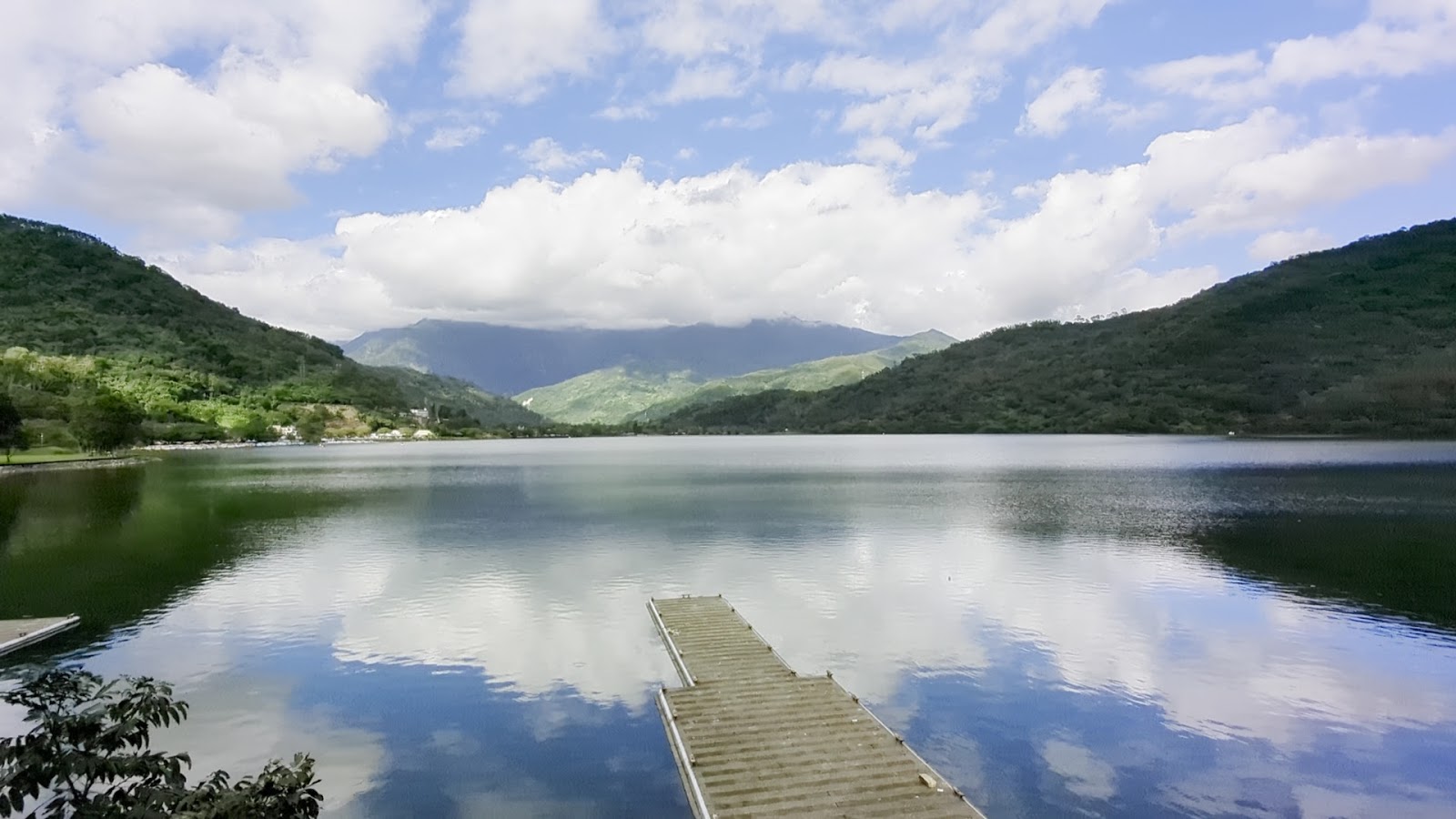 花蓮鯉魚潭晴天湖面如鏡，藍天白雲倒映水中，木棧橋靜靜伸入湖面