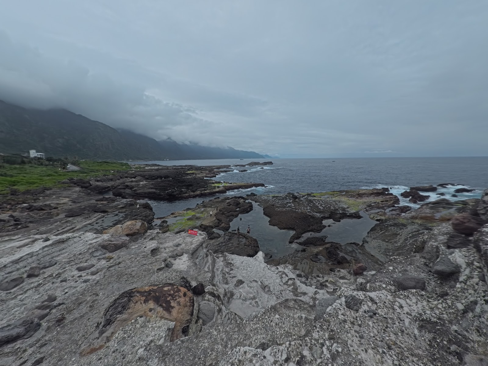 石梯坪海蝕平台岩岸全景，灰色岩盤延伸入太平洋，背景山壁雲霧