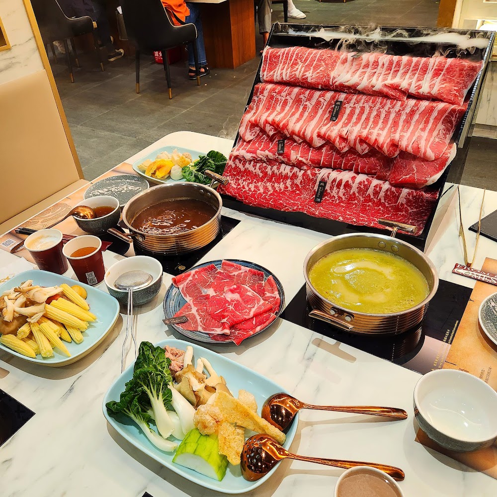 火鍋餐桌上有牛肉片、蔬菜拼盤、玉米與兩種湯底。